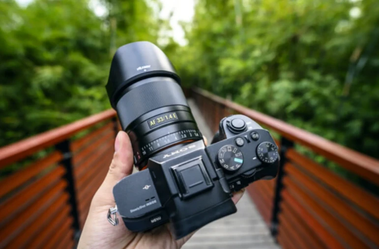 Об'єктив Viltrox AF 33mm f/1.4 E з металевим корпусом і золотистою планкою маркування, встановлений на чорну камеру Sony в руці фотографа