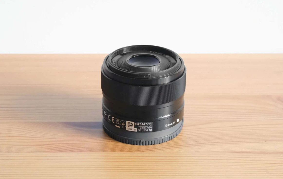 Компактний об'єктив Sony E 35mm f/1.8 OSS крупним планом на дерев'яному столі з чітким маркуванням Optical SteadyShot та діаметром різьби 49 мм